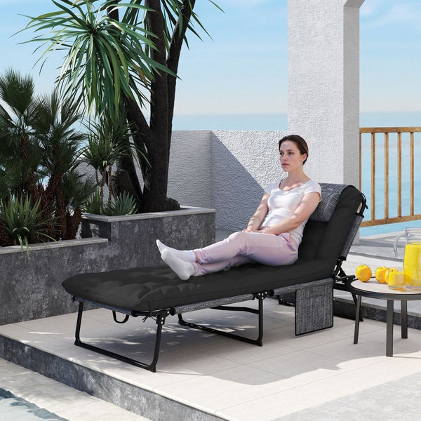 Frau auf einer schwarzen Gartenliege auf einer hellen Terrasse mit Meerblick und Palmen.