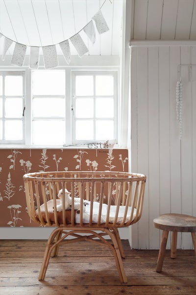 Babyzimmer mit Gitterbett aus Rattan, Holzstuhl und Blumendesign-Tapete
