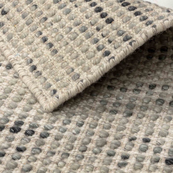 Nahaufnahme eines gewebten Teppichs mit grau-beiger Noppenstruktur und umgeschlagener Ecke