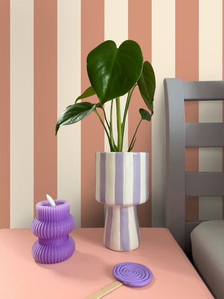 Dekorative Szene mit Pflanze in einem gestreiften Topf, einer geformten Kerze und einem Lutscherstab