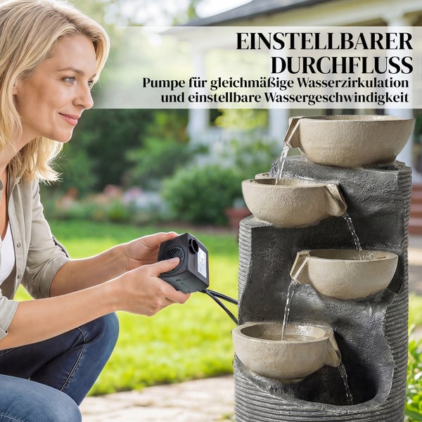 Frau hält Pumpe für einen Gartenbrunnen mit mehreren Schalen und fließendem Wasser zur Einstellung des Durchflusses.