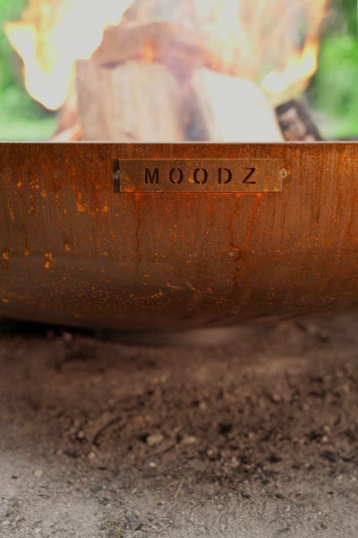 Nahaufnahme einer rostigen MOODZ Feuerschale aus Metall mit brennendem Holz.
