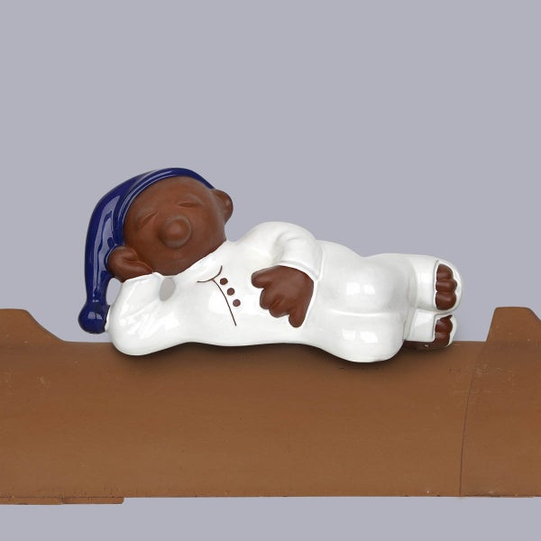 Firststeher Dachfigur schlafendes Männchen in weißem Schlafanzug und blauer Schlafmütze auf einem Dachziegel.