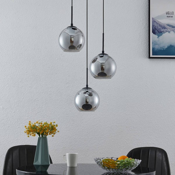 Drei moderne Pendelleuchten mit kugelförmigen, reflektierenden Glasschirmen in einem hellen Esszimmer über einem Tisch mit Blumen und Obstschale.