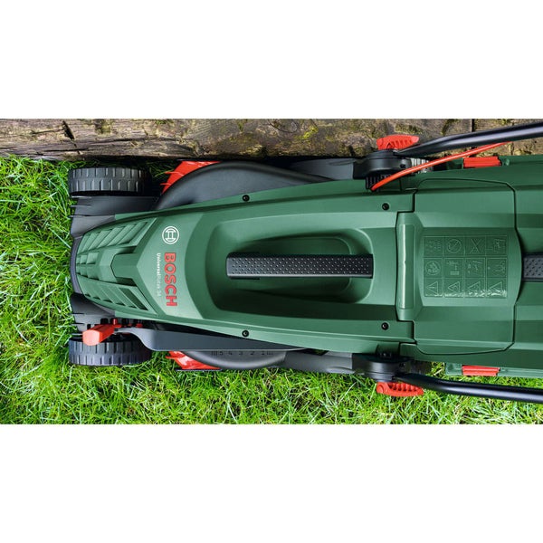 Draufsicht auf einen Bosch Rasenmäher beim Mähen von Gras entlang einer hölzernen Kante im Garten.