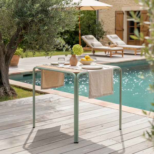 Quadratischer Gartentisch mit hellgrünem Metallgestell und Holzlatten auf einer Terrasse neben einem Pool.