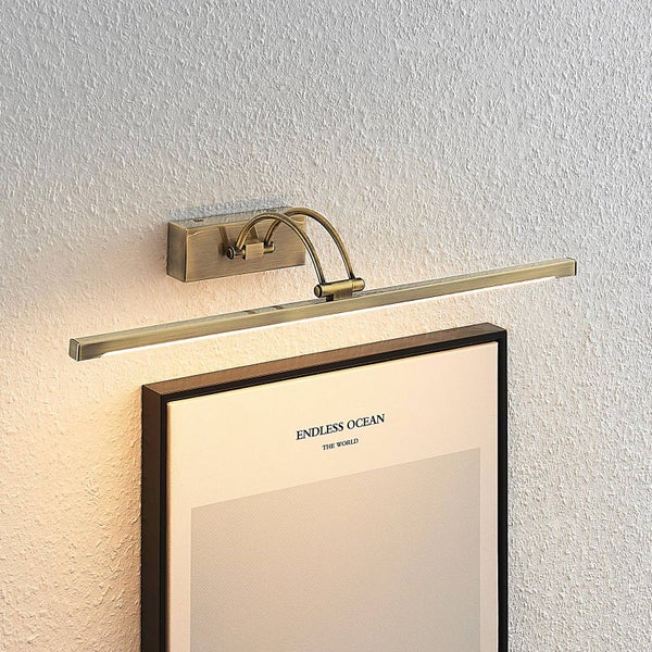 LED-Bilderleuchte aus Messing an einer Wand über einem gerahmten Bild montiert.