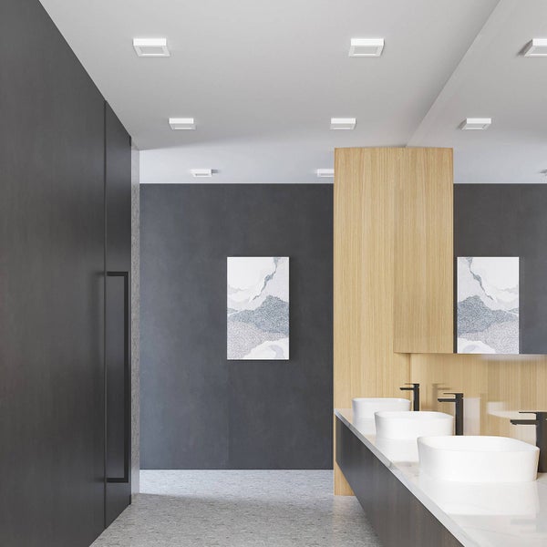 Modernes Badezimmer mit quadratischen LED-Einbaustrahlern an der Decke, drei weißen Aufsatzwaschbecken und Wänden aus Holz und dunklem Putz.