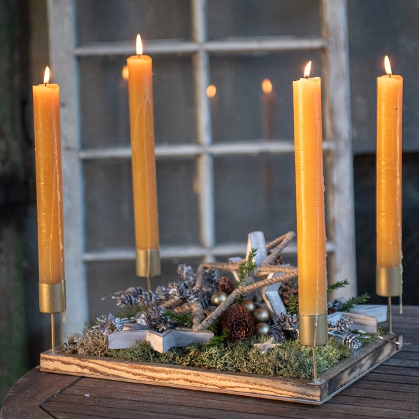 Adventsgesteck mit vier brennenden Kerzen, Sternen und Tannenzapfen auf einem Holztisch