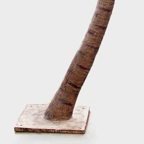 Künstlicher Palmenstamm mit strukturierter Rinde auf quadratischer Bodenplatte.