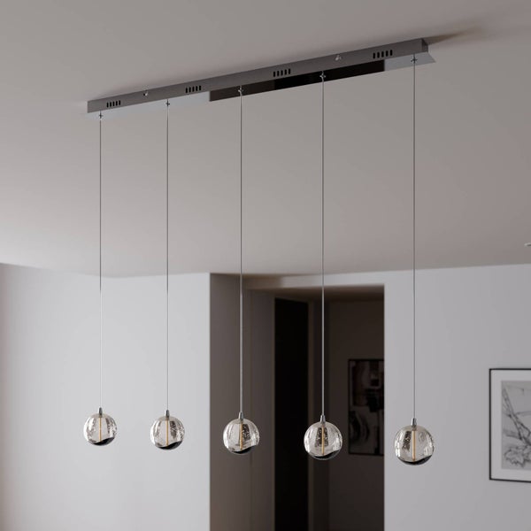 Moderne fünf-flammige Pendelleuchte mit Glasschirmen in Kugelform an einer rechteckigen Metallhalterung in einem hellen Raum.