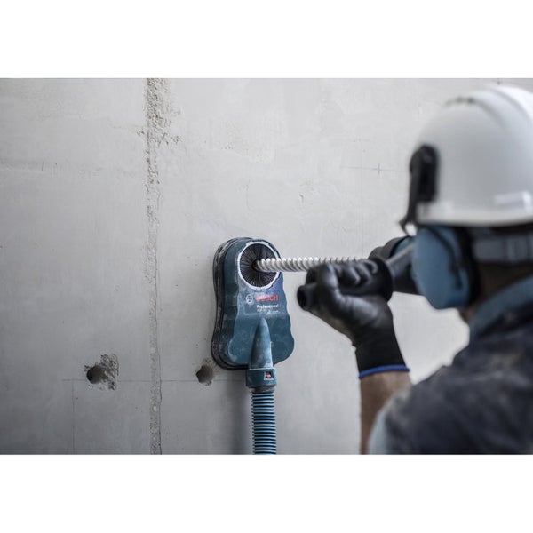 Ein Handwerker bohrt mit einem Bohrhammer und Staubabsaugung ein Loch in eine Wand