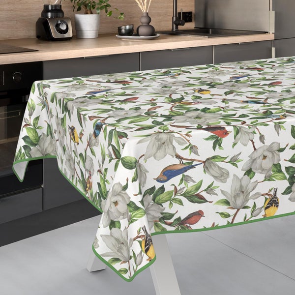 Tischdecke mit floralem Magnolien- und Vogelmuster auf weißem Hintergrund, mit grünem Saum, in einer hellen, modernen Küche.