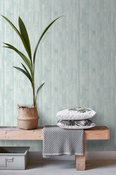 Szene mit Pflanze in einem Korb, Kissen und einer Decke auf einer Holzbank vor einer Wand mit Holzpaneel-Tapete.