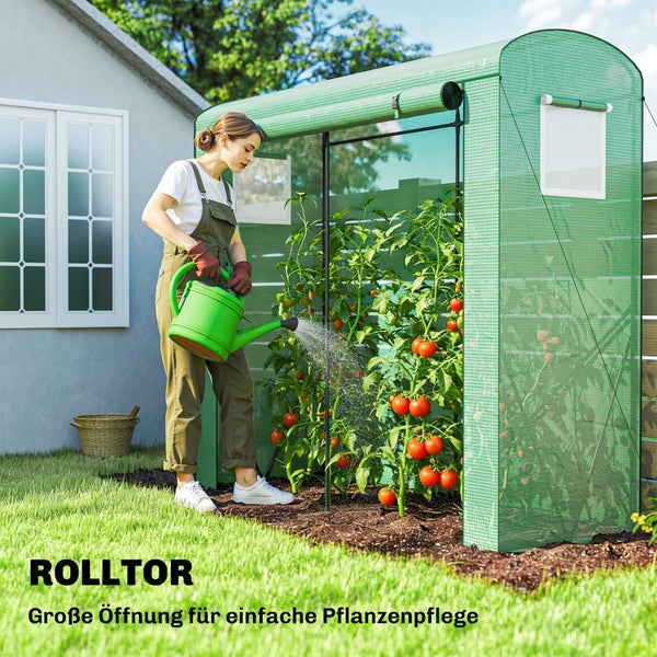 Eine Frau gießt Tomatenpflanzen in einem Kleingewächshaus mit offenem Rolltor in einem Garten.