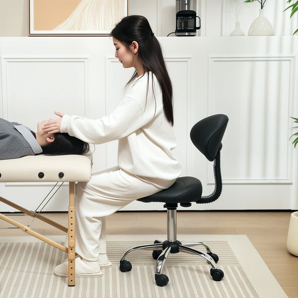 Szene mit einer Person, die auf einem Massagetisch liegt, und einer anderen Person, die auf einem Sattelhocker sitzt