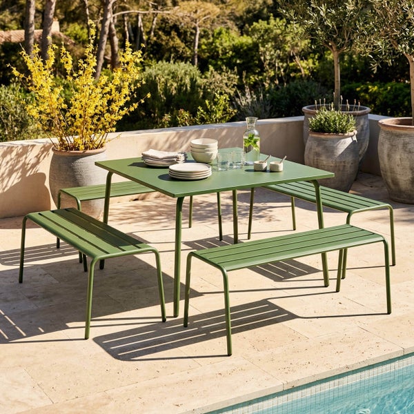 Grünes Gartenmöbel-Set aus Metall mit quadratischem Tisch und vier Bänken auf einer hellen Steinterrasse neben einem Pool.