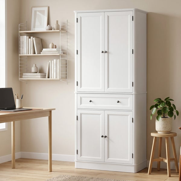 Hoher weißer Schrank mit vier Türen und einer Schublade in einem hellen Arbeitszimmer neben einem Schreibtisch und Wandregal.