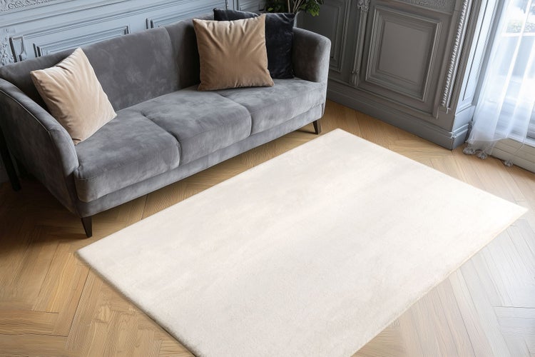 Ein rechteckiger, unifarbener Wohnzimmerteppich liegt auf einem Holzboden vor einem Sofa in einem elegant eingerichteten Wohnbereich.