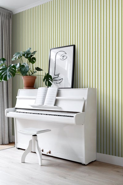 Szene mit weißem Klavier, Hocker, Zimmerpflanze und gerahmtem Bild vor einer gestreiften Tapete.