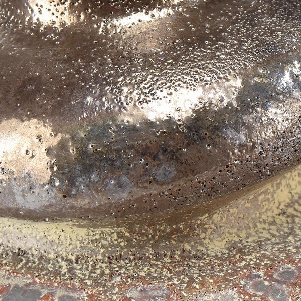 Nahaufnahme einer rauen, metallischen Oberfläche mit vielen kleinen Löchern.