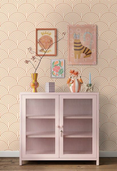 Tapete mit geometrischem Muster aus konzentrischen Bögen im Art-déco-Stil, dargestellt in einem Raum mit rosa Schrank und Dekorationsobjekten.