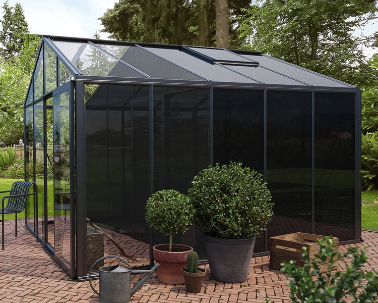 Modernes Gewächshaus mit Aluminiumrahmen und Glasflächen auf einer gepflasterten Terrasse im Garten.