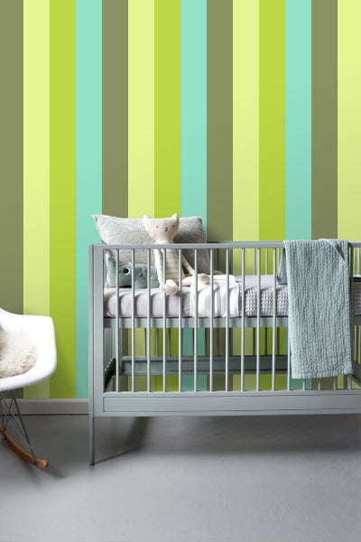 Kinderzimmer mit Babybett, Kissen, Spielzeug und Schaukelstuhl vor gestreifter Tapete