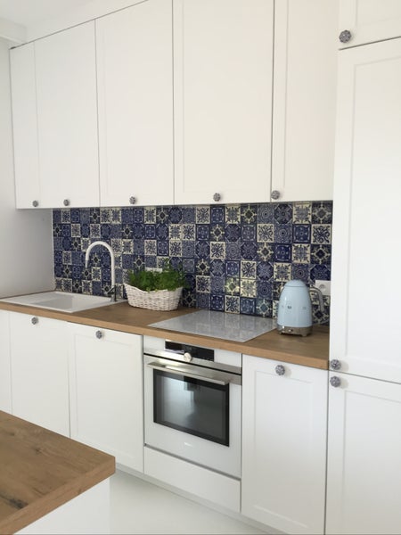 Helle Küche mit weißen Schränken, Arbeitsplatte in Holzoptik und blau gemusterten Fliesen