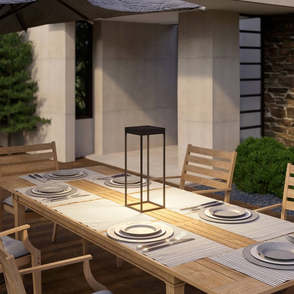 Moderne schwarze Laterne auf einem gedeckten Holztisch in einem organisierten Außenbereich mit Terrasse und Sonnenschirm.