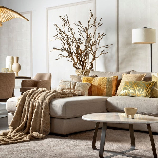 Wohnzimmer-Szene mit Sofa, Kissen, Decke, Tisch und dekorativen Elementen für eine stilvolle Inneneinrichtung.