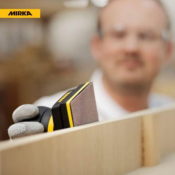 Handwerker schleift mit einem Mirka Handschleifblock eine Holzkante. Mirka Logo sichtbar.