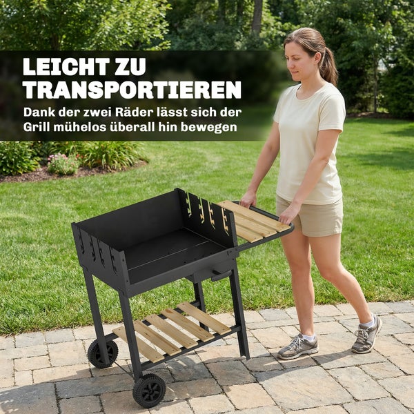 Eine Frau schiebt einen schwarzen Holzkohlegrill mit Holzablagen auf zwei Rädern über eine gepflasterte Fläche im Garten.