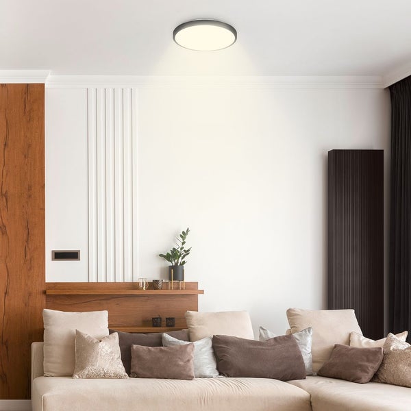 Runde LED-Deckenleuchte in einem modernen, hellen Wohnzimmer mit beigem Sofa und Wandelementen in Holzoptik.
