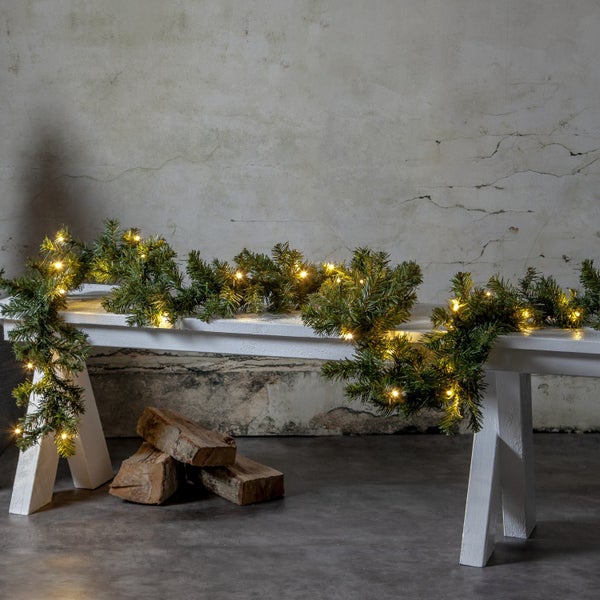 Dekorierte Tannengirlande auf weißer Holzbank neben Brennholz