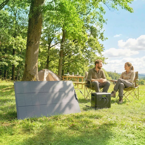 Mobiles Solarpanel und Powerstation im Einsatz beim Camping im Wald mit zwei Personen auf Klappstühlen.