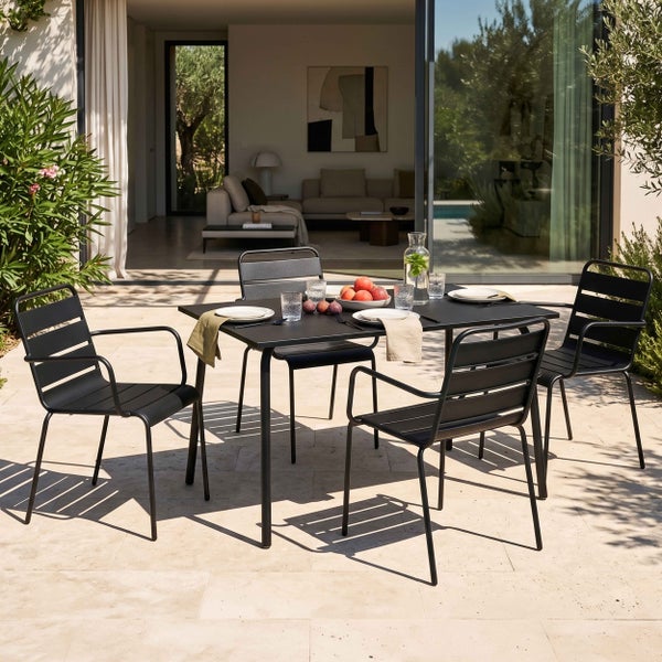 Moderner Esstisch für den Garten aus Metall mit vier Armlehnenstühlen auf einer hellen Terrasse aus Naturstein.