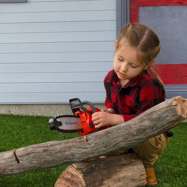 Mädchen sägt mit Spielzeugmotorsäge von Husqvarna einen Baumstamm