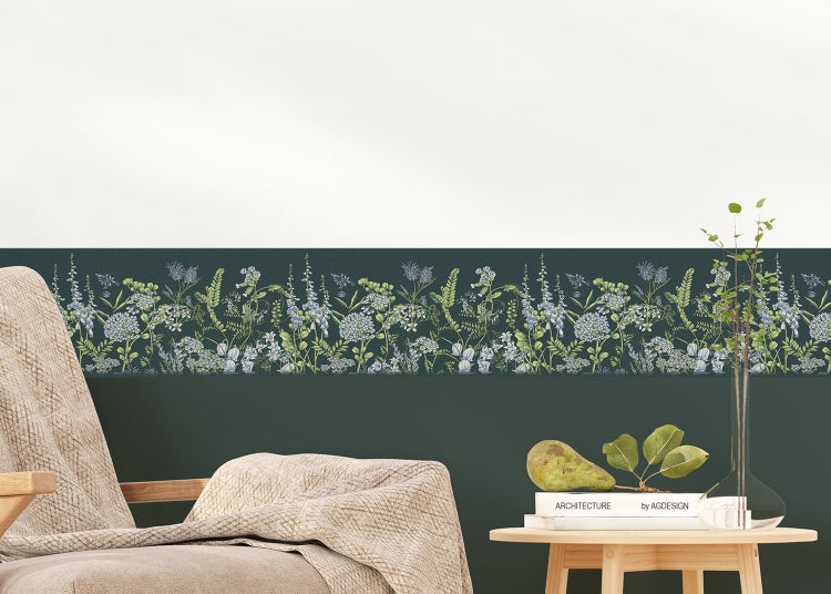 Tapetenbordüre mit Wiesenblumen-Dekor an einer Wand in einem hellen Zimmer mit Sessel und Beistelltisch aus Holz.