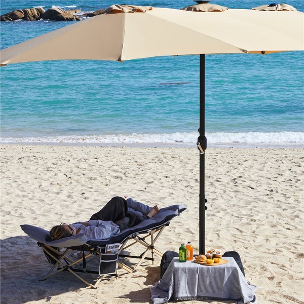 Großer beiger rechteckiger Sonnenschirm und ein grau gepolstertes Feldbett an einem hellen Sandstrand am Meer.