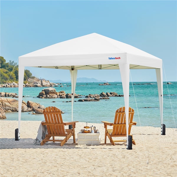 Weißes Faltzelt mit zwei Holzstühlen am Strand