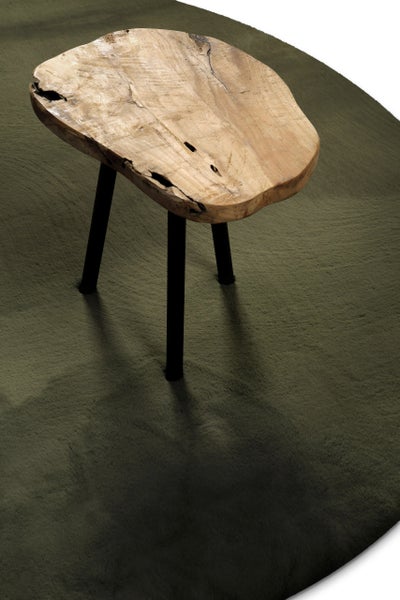 Beistelltisch aus Massivholz mit unregelmäßiger Platte und drei schwarzen Beinen auf einem runden Teppich.