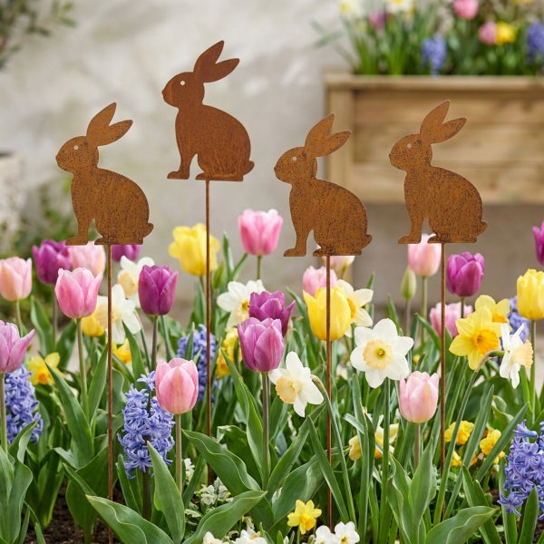 Vier Hasen als Gartenstecker aus Edelrost in einem frühlingshaften Blumenbeet mit Tulpen und Narzissen.