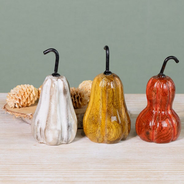 Drei dekorative Kürbisse aus Holz mit metallischem Stiel als Herbstdekoration auf einem Holztisch.