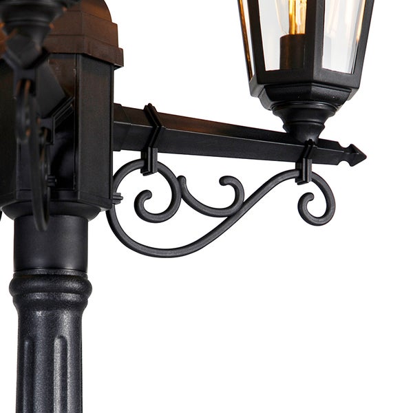 Detailansicht eines schwarzen Außenlampenmasts mit dekorativen Verzierungen und einer Laterne im traditionellen Stil.