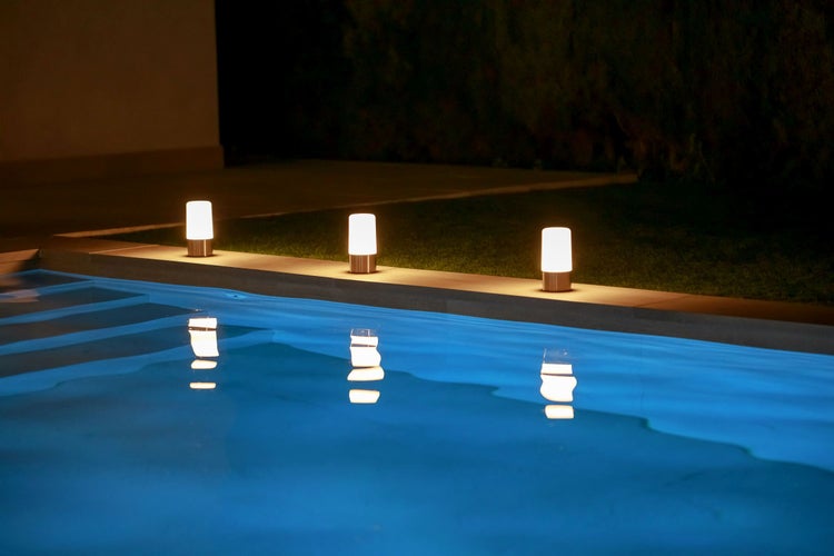 Drei zylindrische LED Außenleuchten am beleuchteten Swimmingpool im Garten bei Nacht mit Lichtreflexionen auf der Wasseroberfläche.