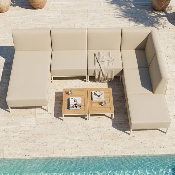 Modernes Garten-Lounge-Set bestehend aus Ecksofa mit Recamiere und zwei Couchtischen aus Holz auf einer Terrasse am Pool.