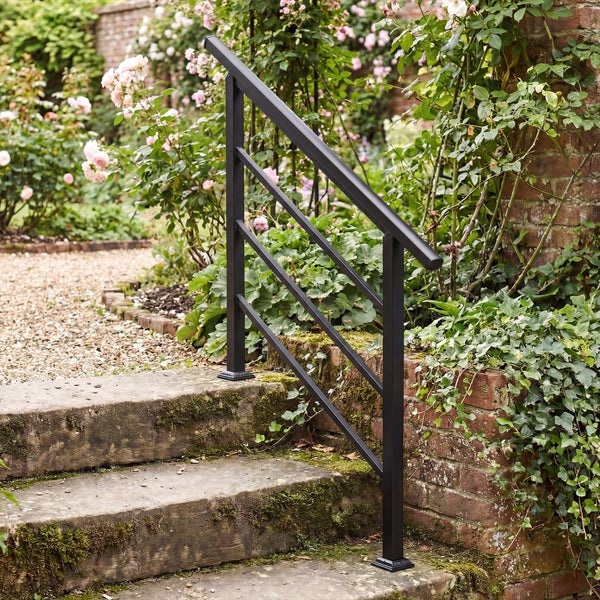 Schwarzer Metall-Handlauf an einer Steintreppe in einem gepflegten Garten mit Blumen und Ziegelmauer.