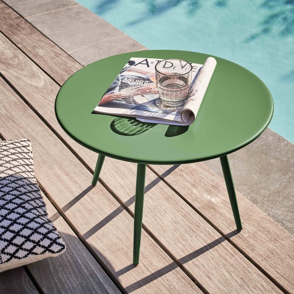 Runder Beistelltisch aus Metall in Grün auf einer Holzterrasse am Pool mit einer Zeitschrift und einem Glas Wasser.