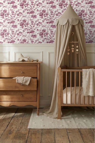 Kinderzimmer mit Blumentapete, weißer Wandtäfelung, Babybett aus Holz mit Baldachin und Holzkommode auf Dielenboden.